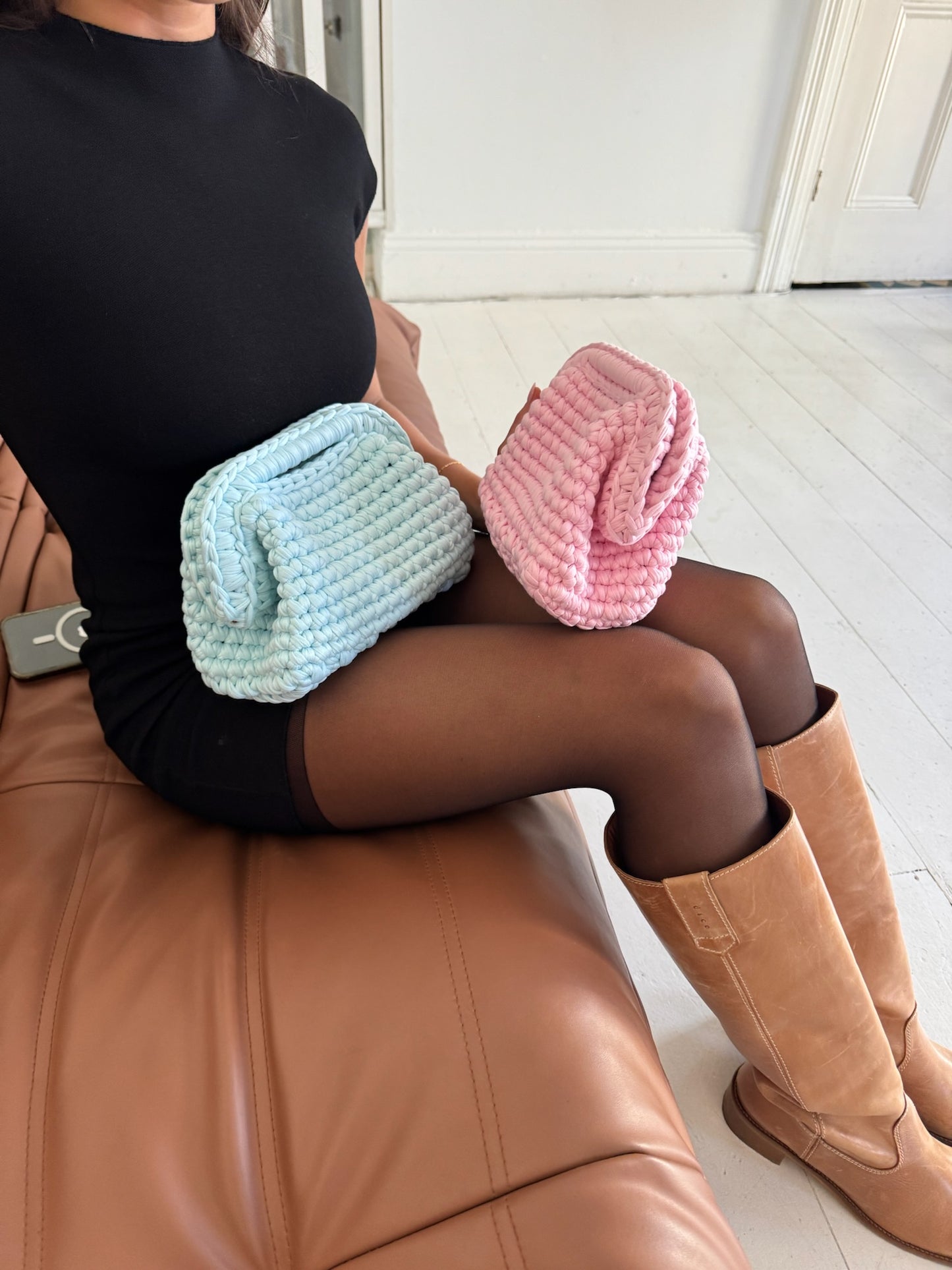 Person sitting on a brown leather chair with two colorful crochet bags on their lap.
