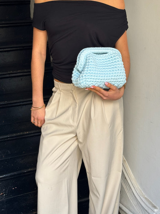 Person holding a light blue knitted clutch bag against a neutral background